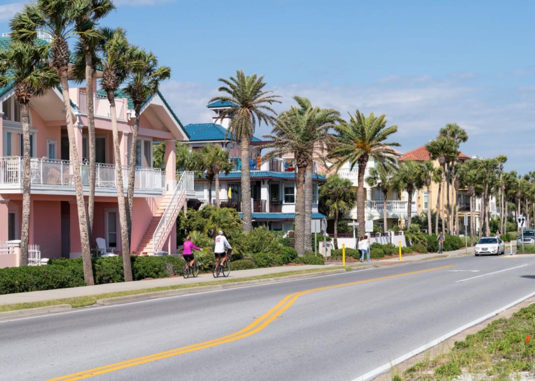 People walking and riding bicycles alongside palm trees and colorful homes.