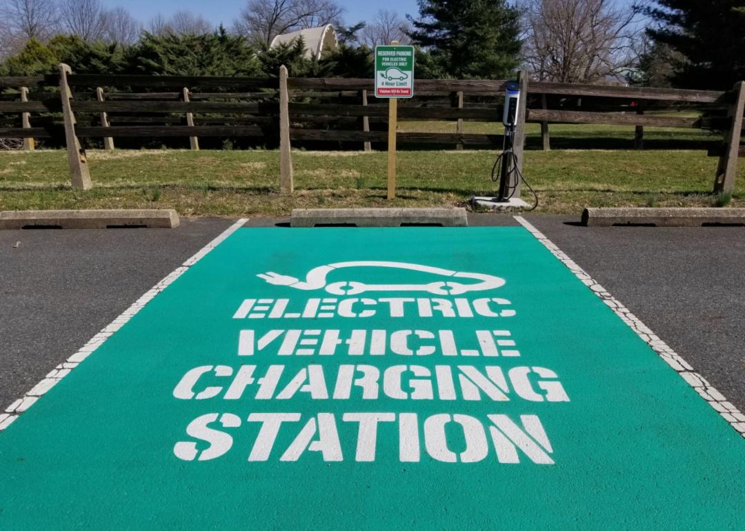 A designated green parking spot for electric vehicle charging station in front of a black fence.