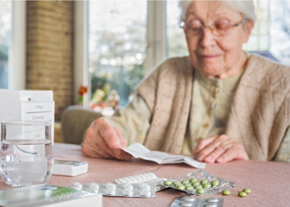 An elderly woman sitting at a table with medication in front of her.