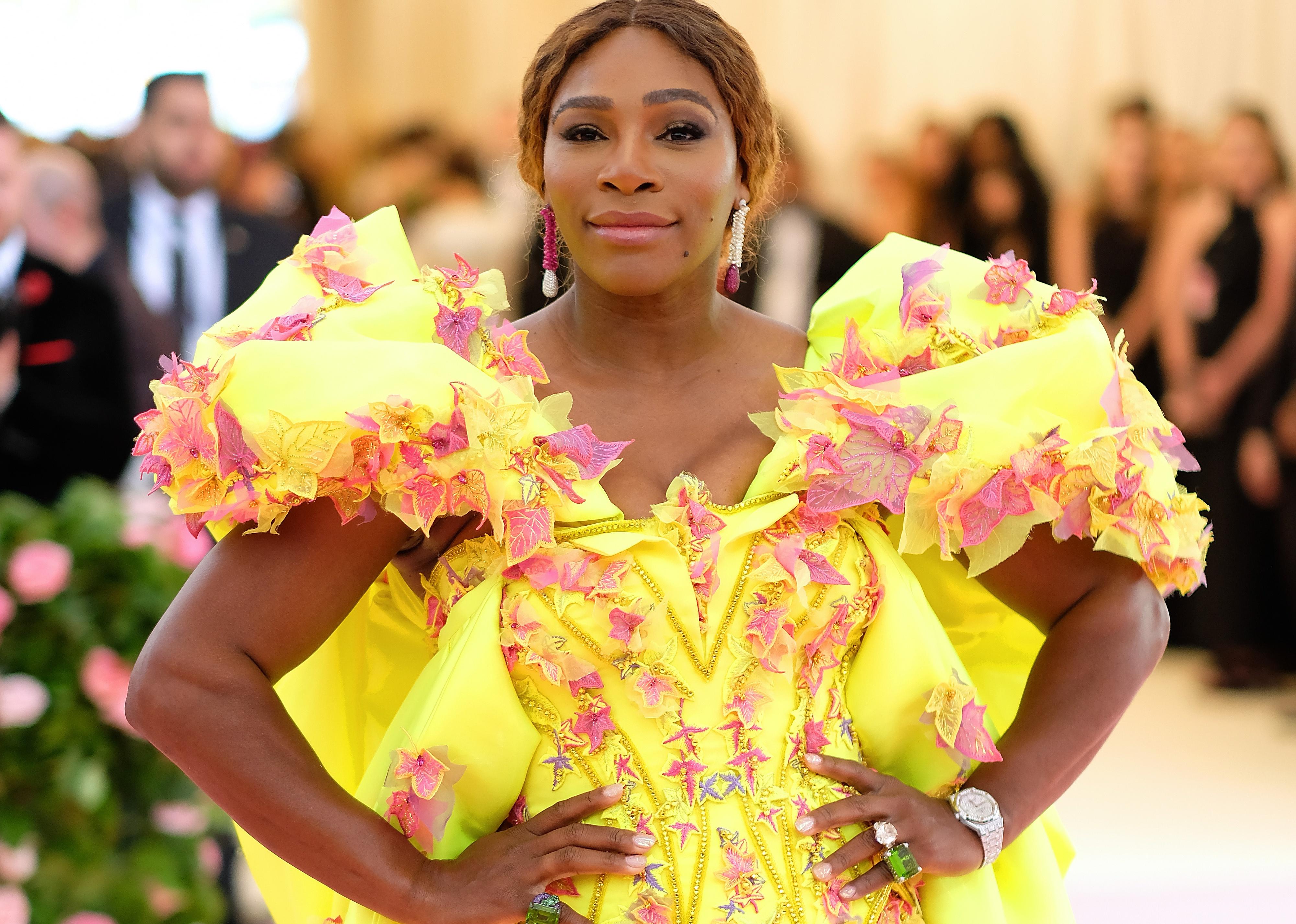 Serena Williams in a bright yellow and pink gown with an engagement ring on and a large green ring.