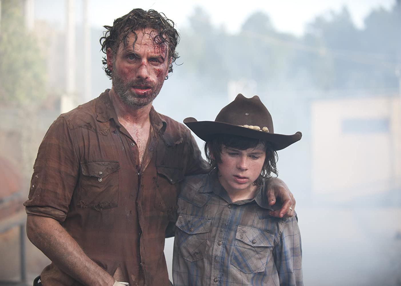 Andrew Lincoln, looking very beat up, holding onto a boy wearing a cowboy hat.