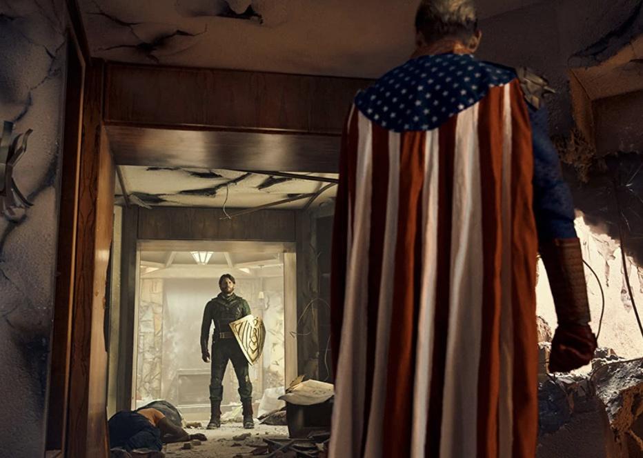 Two superheroes, one with an american flag cape and the other with a shield, facing eath other in the hallway of a destroyed building