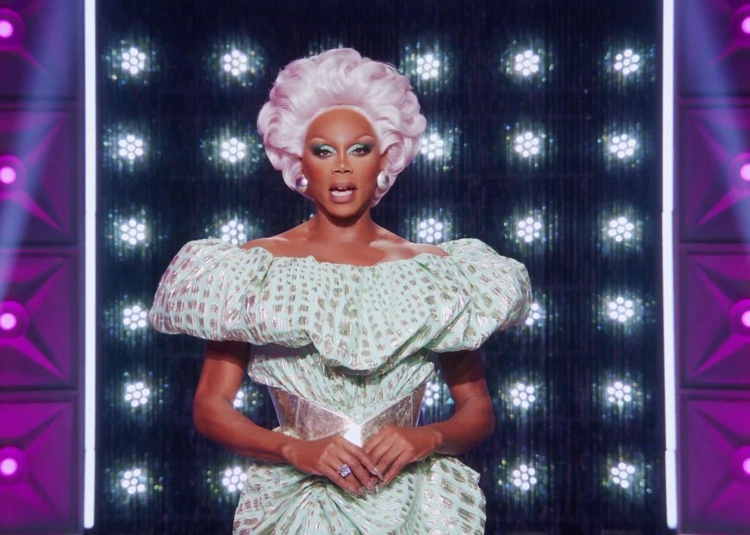 RuPaul, wearing a short purple wig and shiny gown, onstage.