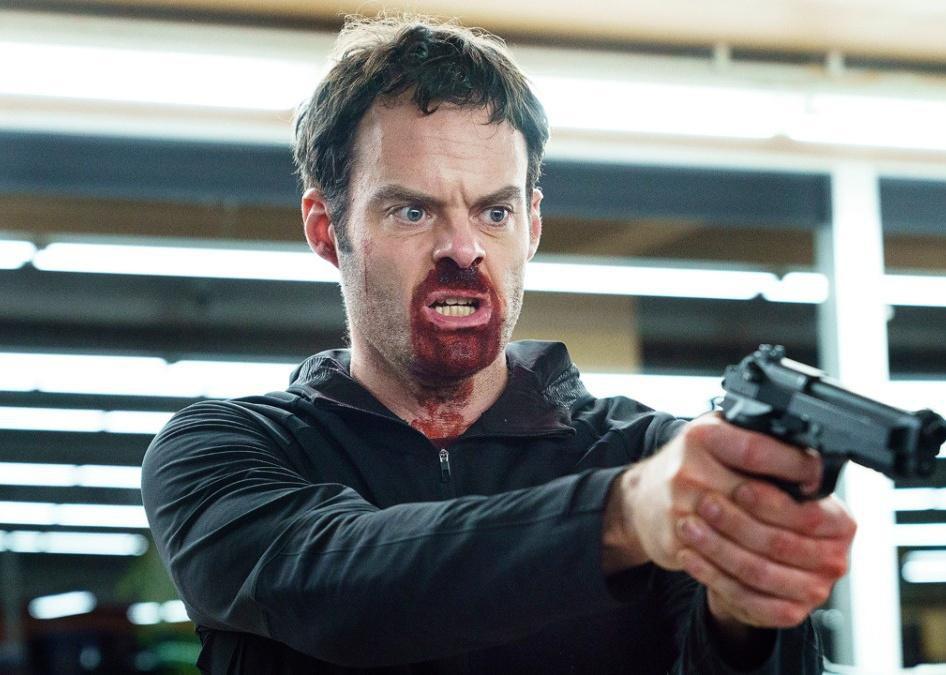 Bill Hader holding a gun with blood on his face.