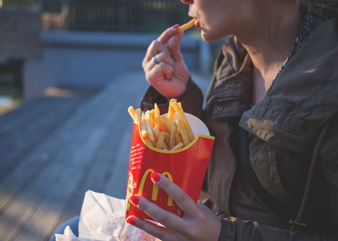 A woman in a green coat eating McDonald's fries.