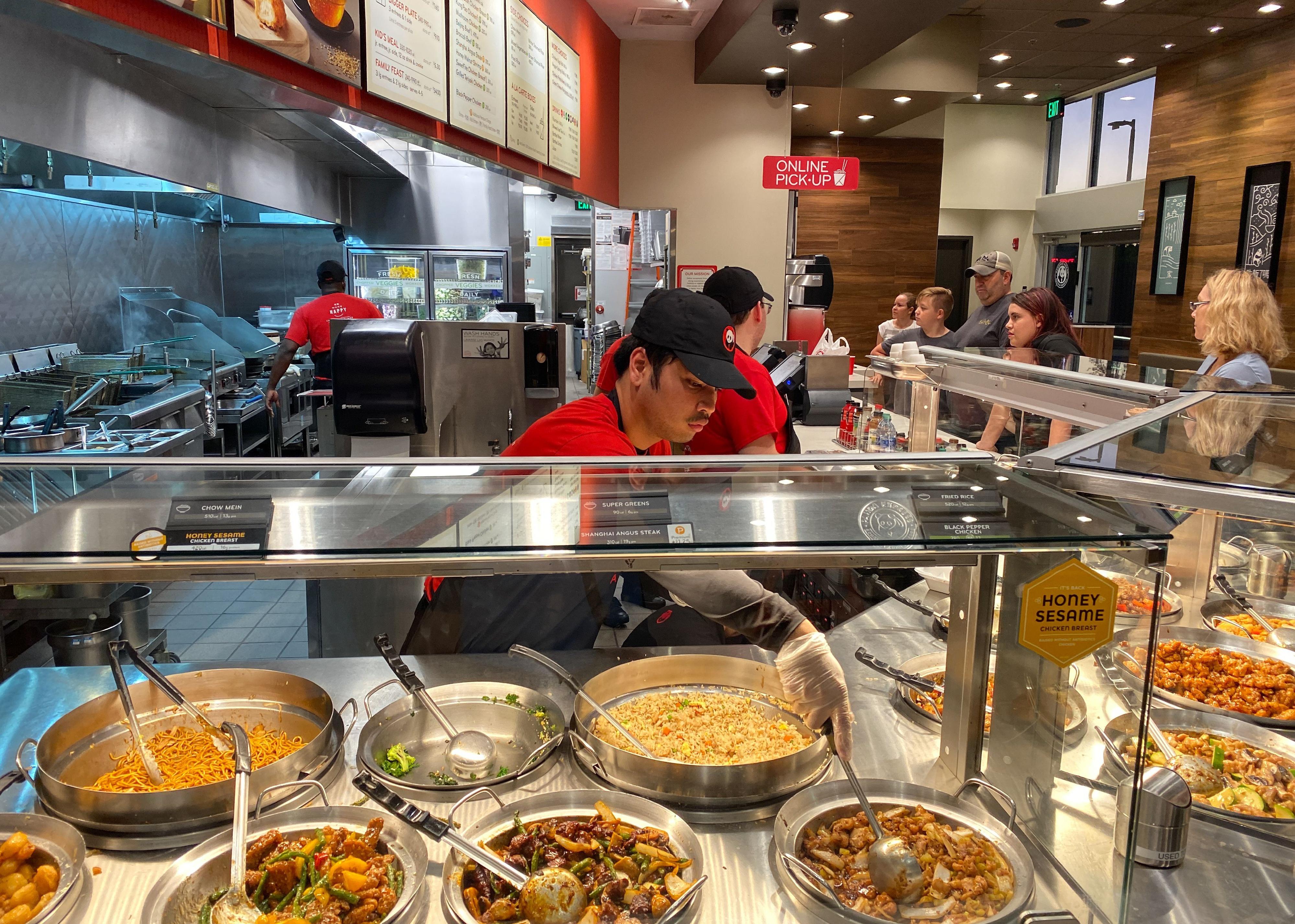 People standing in line ordering while Panda Express employees serve plates.
