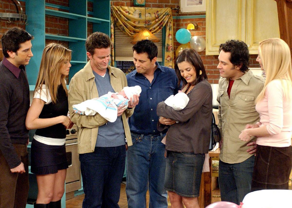 Jennifer Aniston, Courteney Cox, Lisa Kudrow, Matt LeBlanc, Matthew Perry, David Schwimmer, and Paul Rudd stand together in a kitchen with two babies.