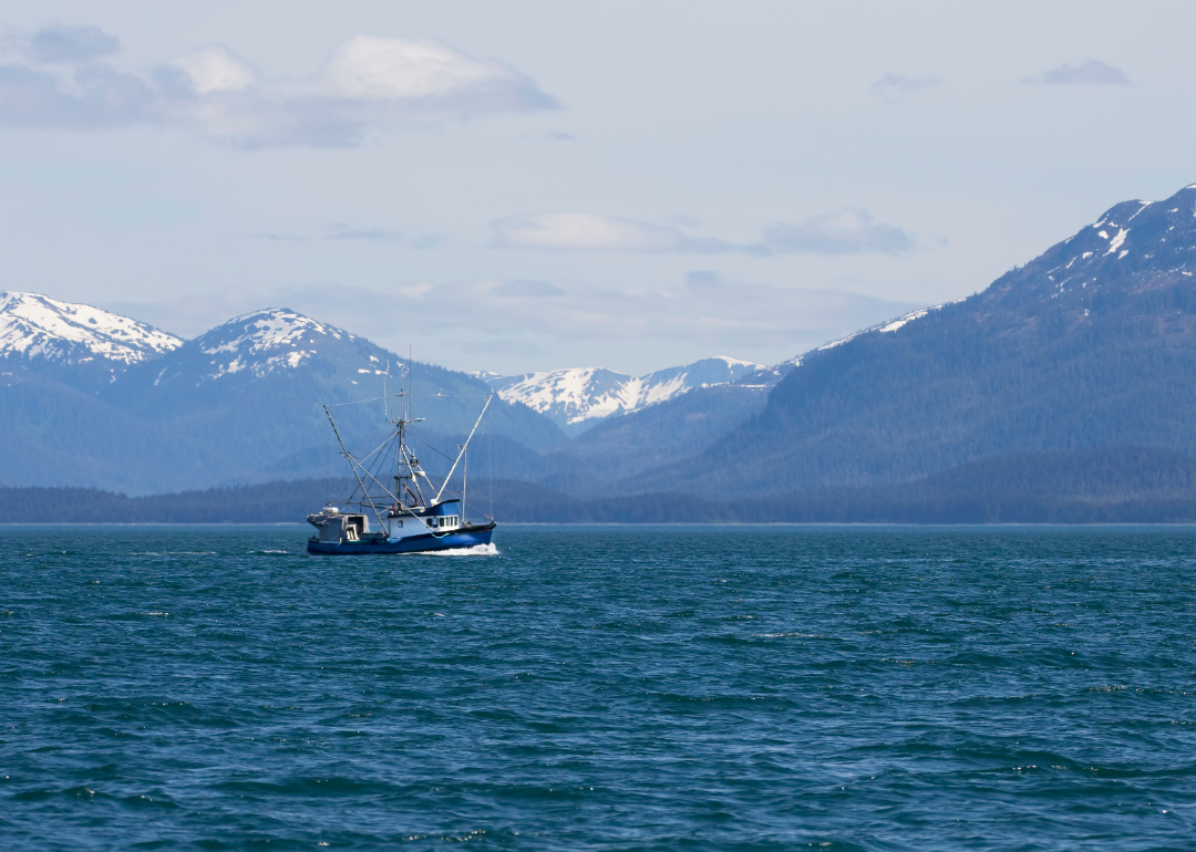 A fishing boat in water with snow topped mountains in the background. 
