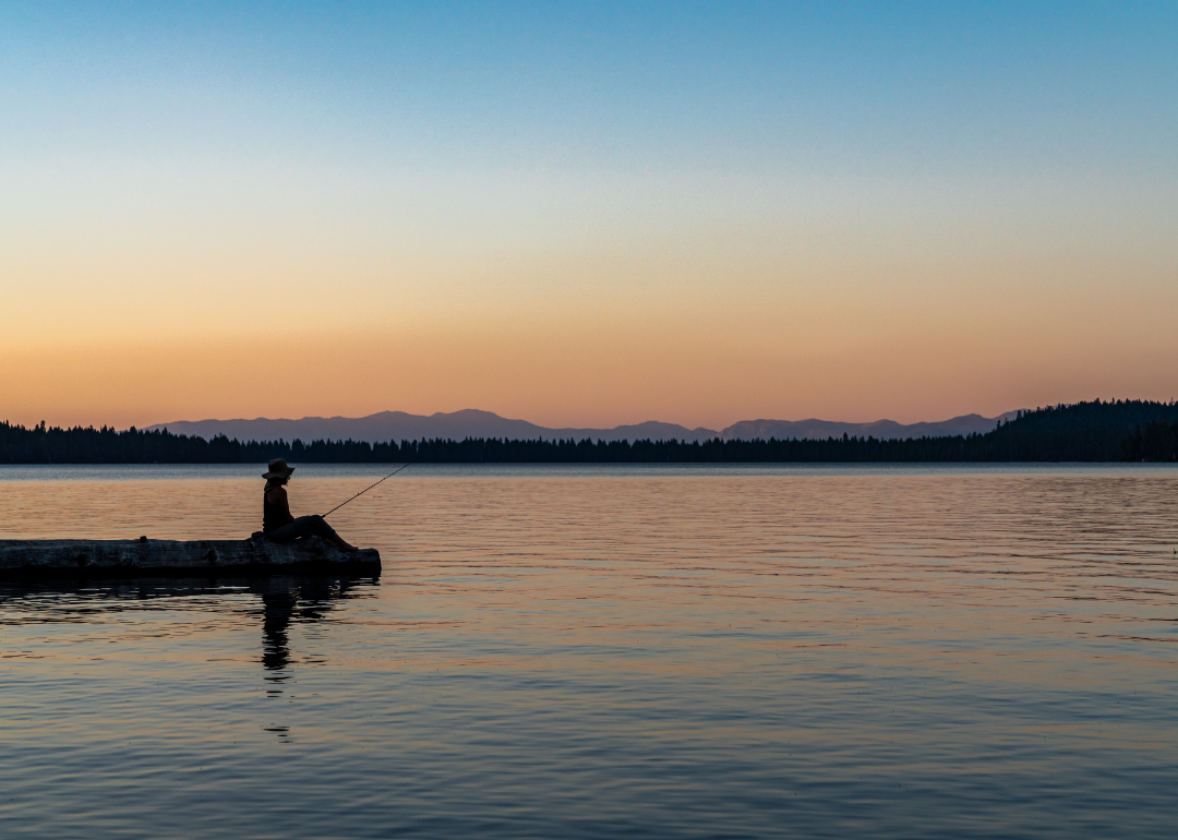 The silhouette of a person sitting on the end of a jetty, fishing at sunset., 