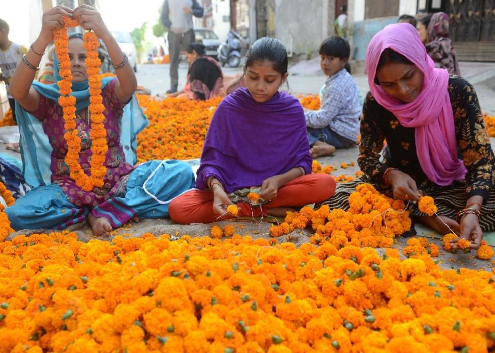 Women and children making garlands while they sit on the ground surrounded by marigolds.