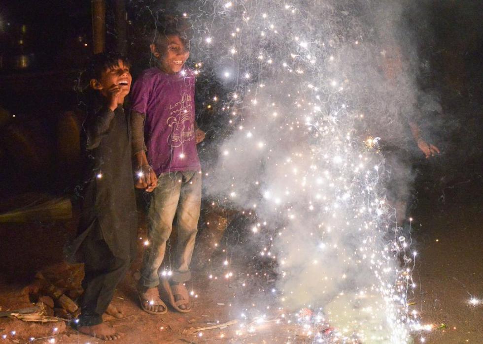 Two young children smiling at a cloud of sparkling firecrackers in front of them.