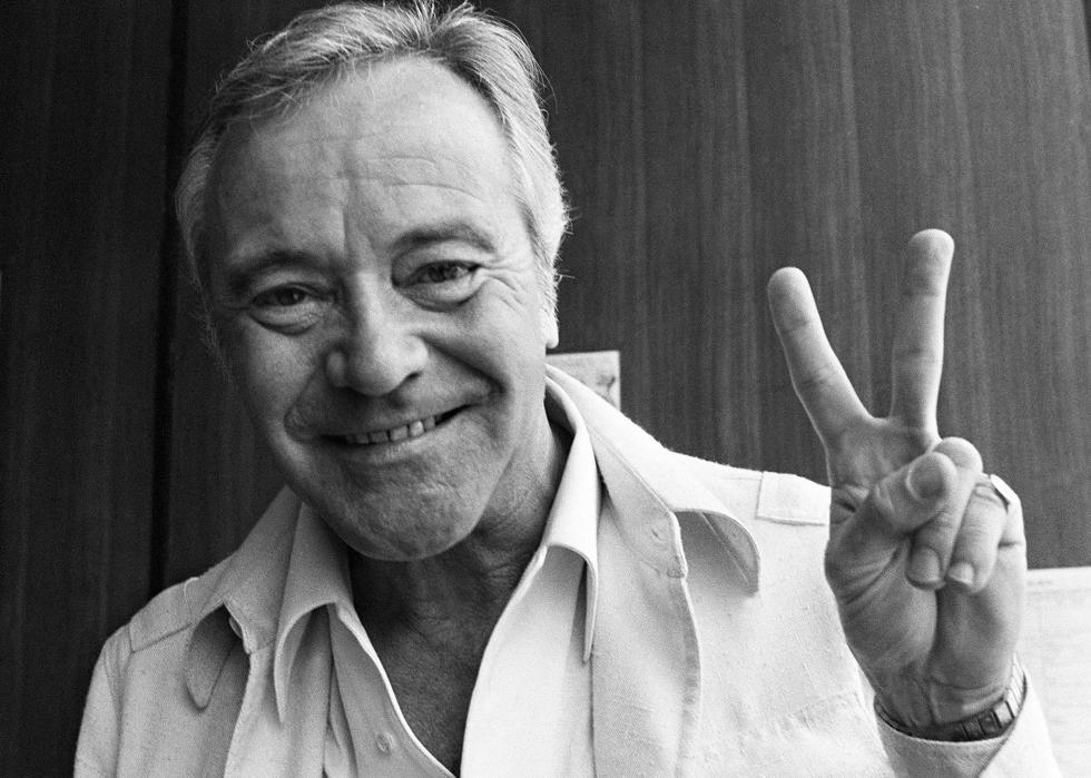 Jack Lemmon smiling, giving the peace sign. 
