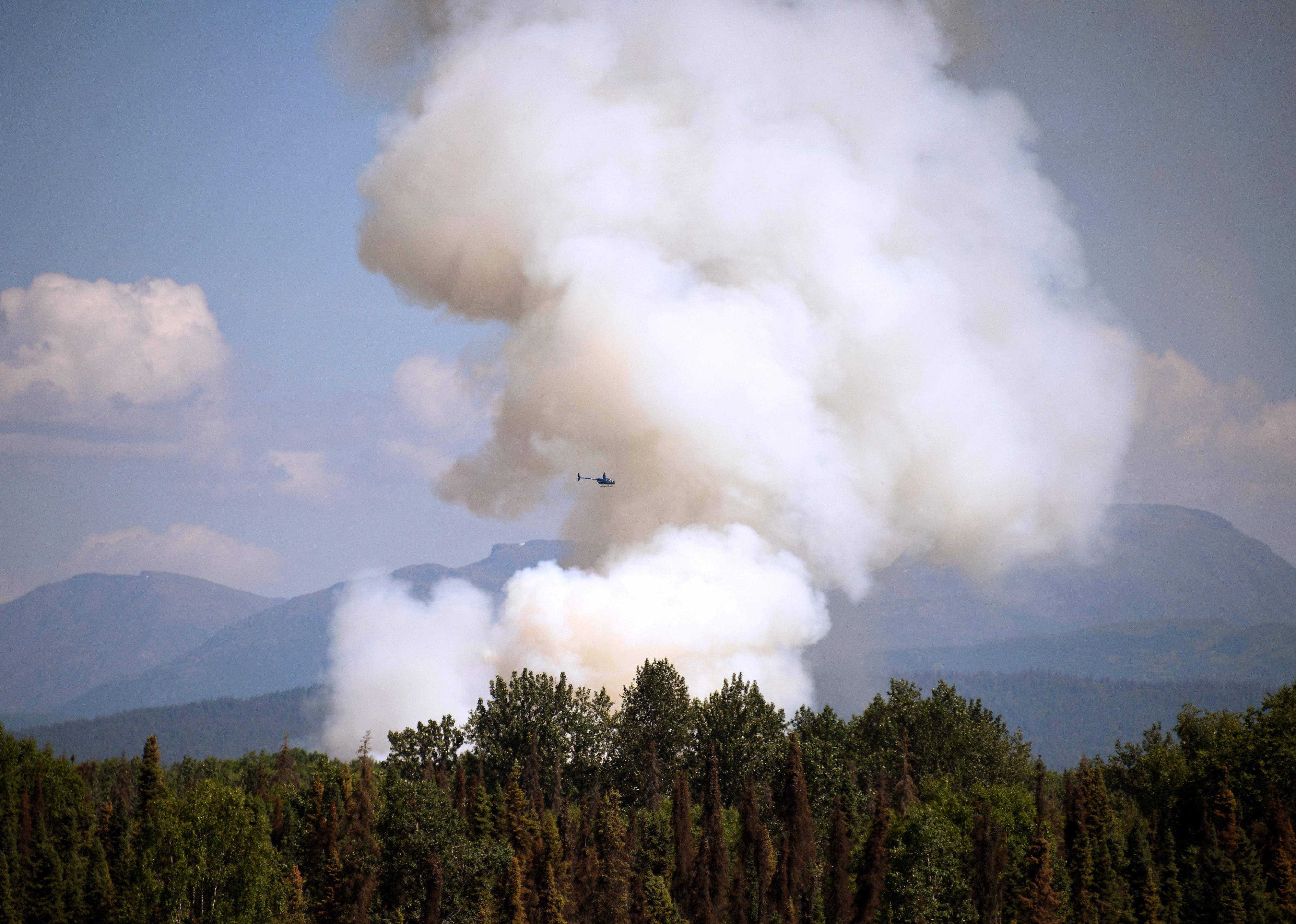 A helicopter passes by as smoke rises from a wildfire.