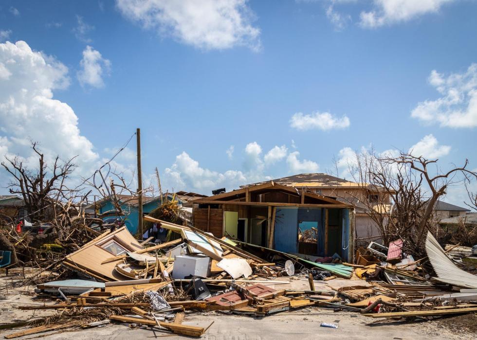 A blue sky with light fluffy clouds over a completely destroyed home surrounded by debris.