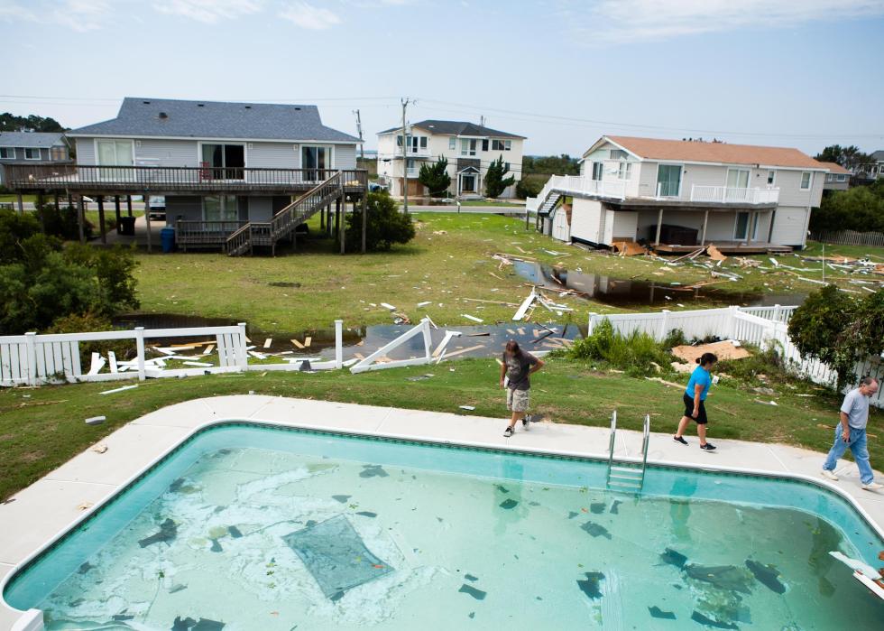 A few people standing near an in-ground pool in a suburban neighborhood that has been hit by a storm.