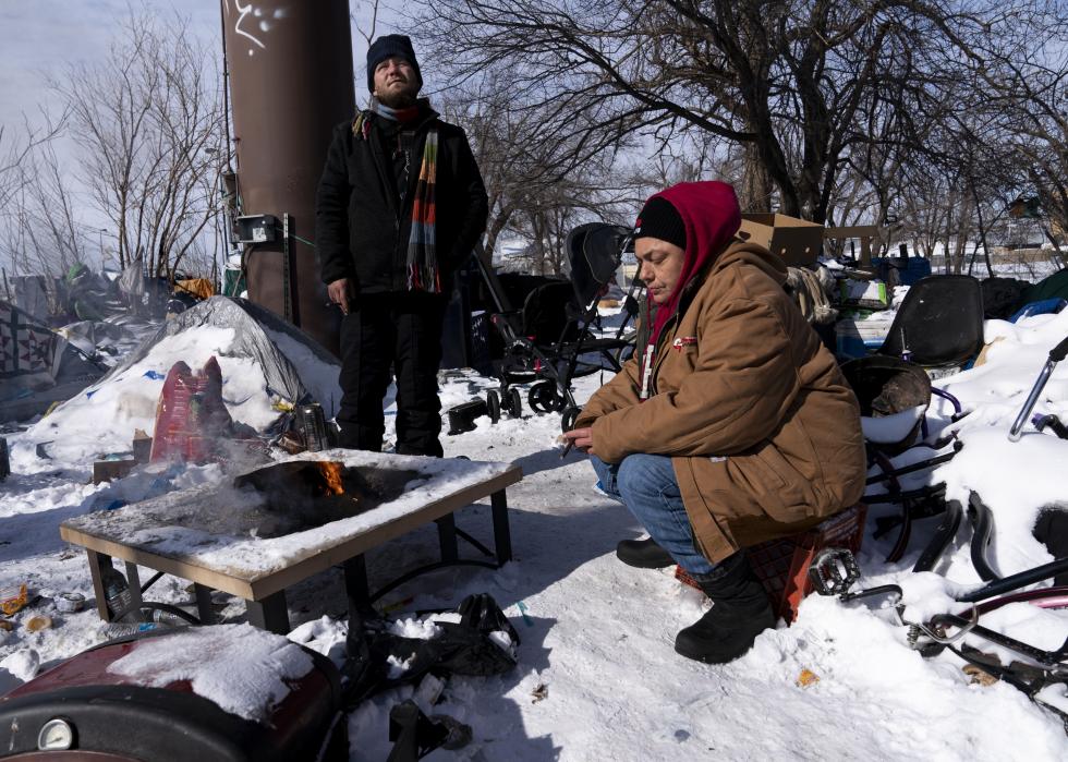 Two people sit around a fire in a snow-covered camp in Oklahoma City.
