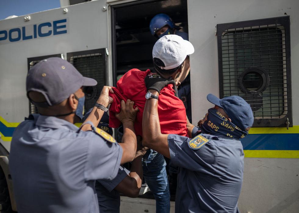 South African Police Service officers force a man inside a police van