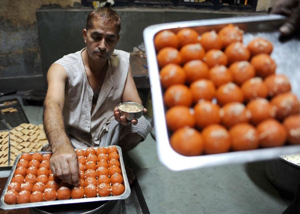 A man preparing trays of gulab jamun, which look like red-orange colored spheres.