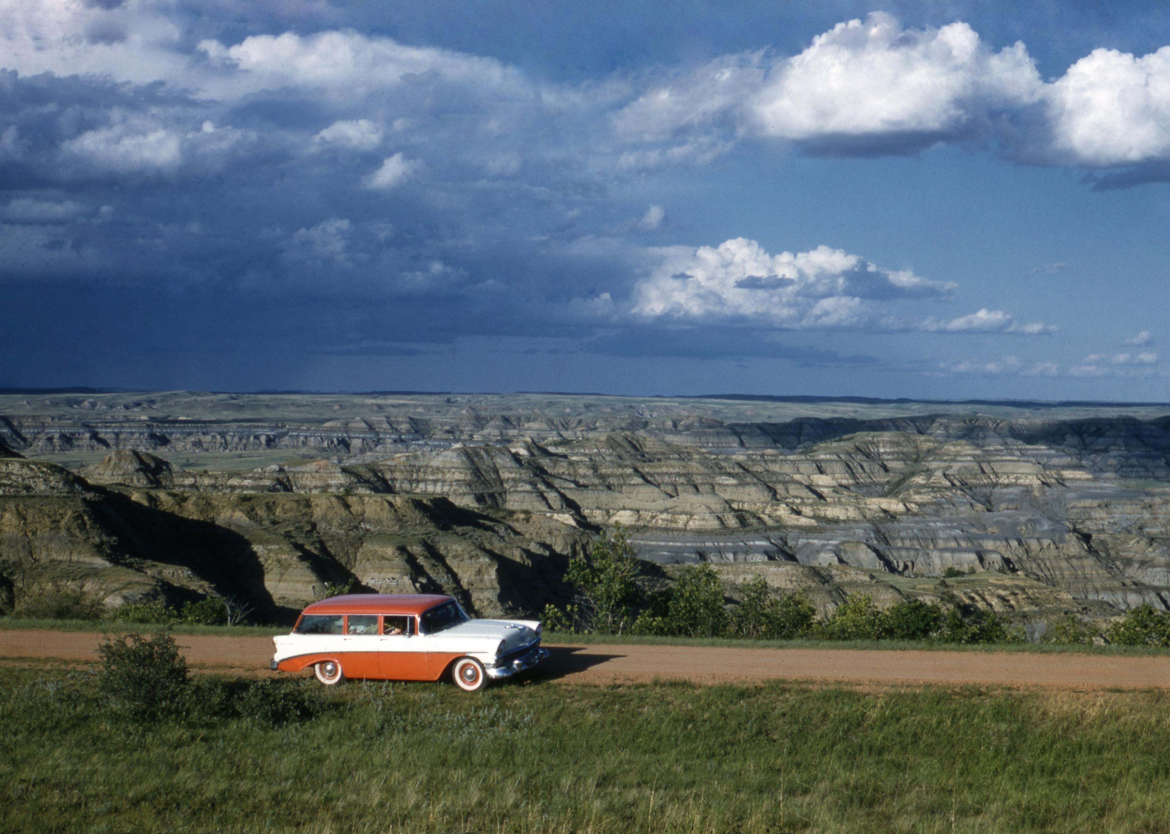 A classic red and white automobile parked on a dirt road.