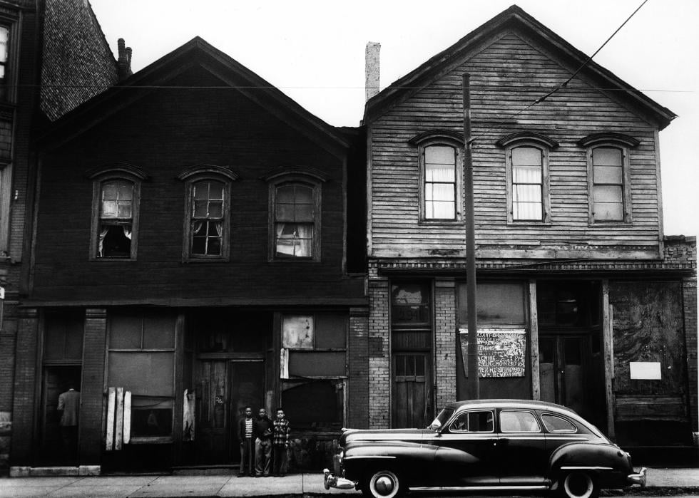 Chicago street with three young children in front of a wood-sided home and a parked car
