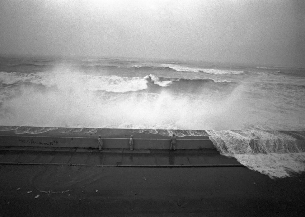 People stand behind a barrier being hit by ocean waves.