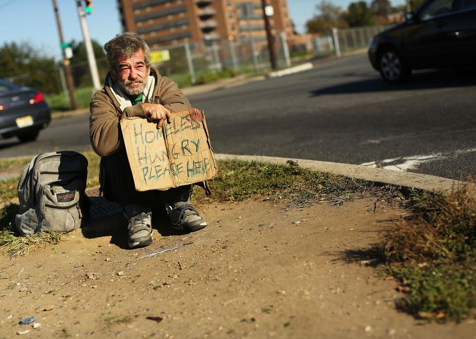 A man holding a sign that says, homeless, hungry, please help, waits for donations from passing motorists in Camden, New Jersey. 