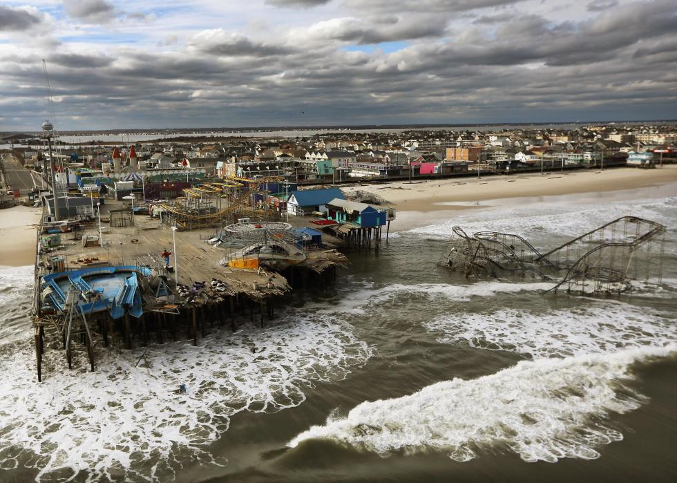 A destroyed amusement park on a pier by the shore in Seaside Heights, New Jersey, with a rollercoaster partially submerged in the ocean.