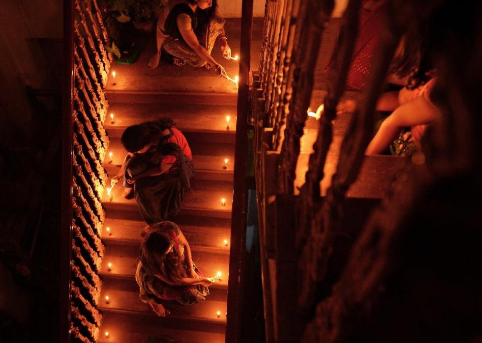 A view from above of people lighting candles that are lining a staircase in a home. 