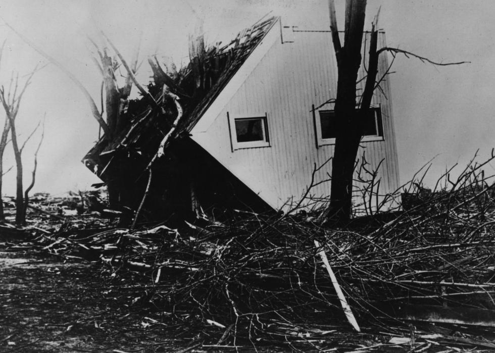 A house on its side surrounded by destroyed trees.