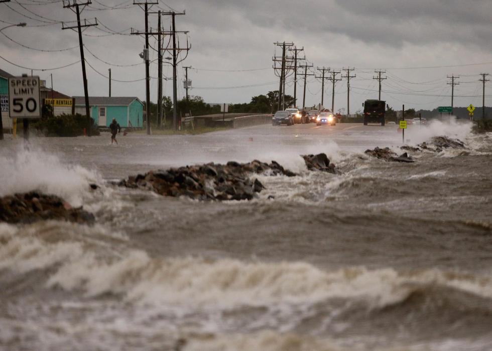 Cars stopped as waves crash over the rocks and onto the road in front of them.