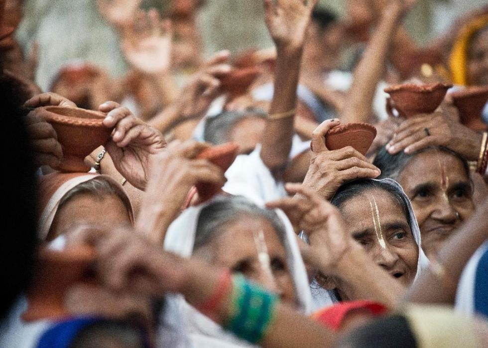 A crowd of older women wearing white and holding diyas (small clay pots) on their heads. 