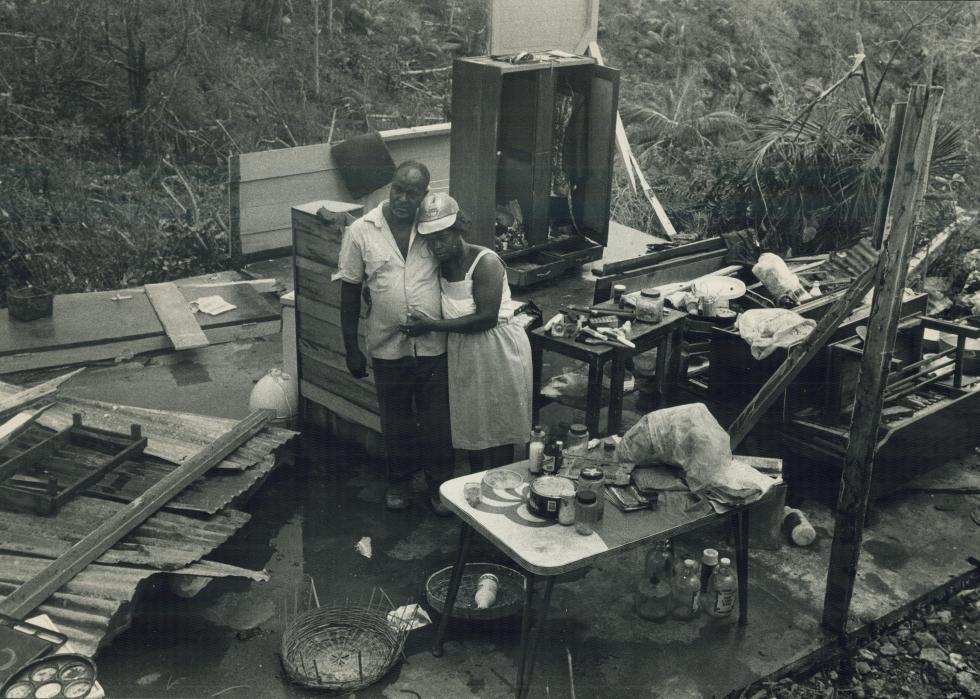 A couple surrounded by debris from a home embrace each other.