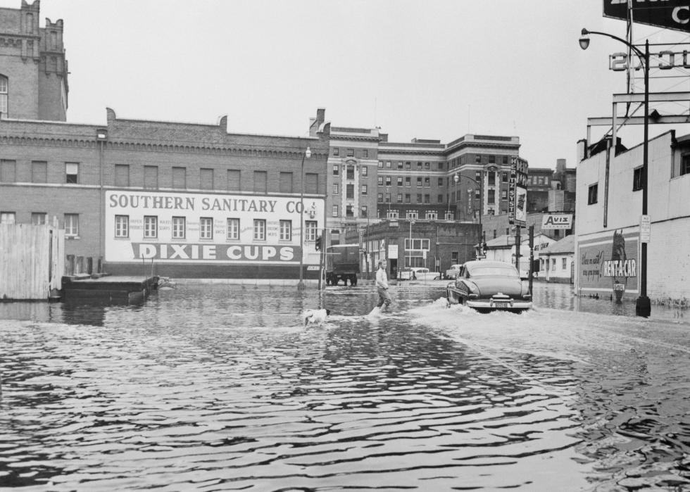 A person walks through a flooded urban area in front of a warehouse for Southern Sanitary Co. Dixie Cups.