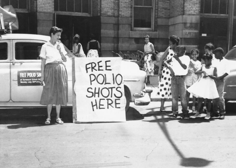 Woman and children standing next to Free Vaccination sign