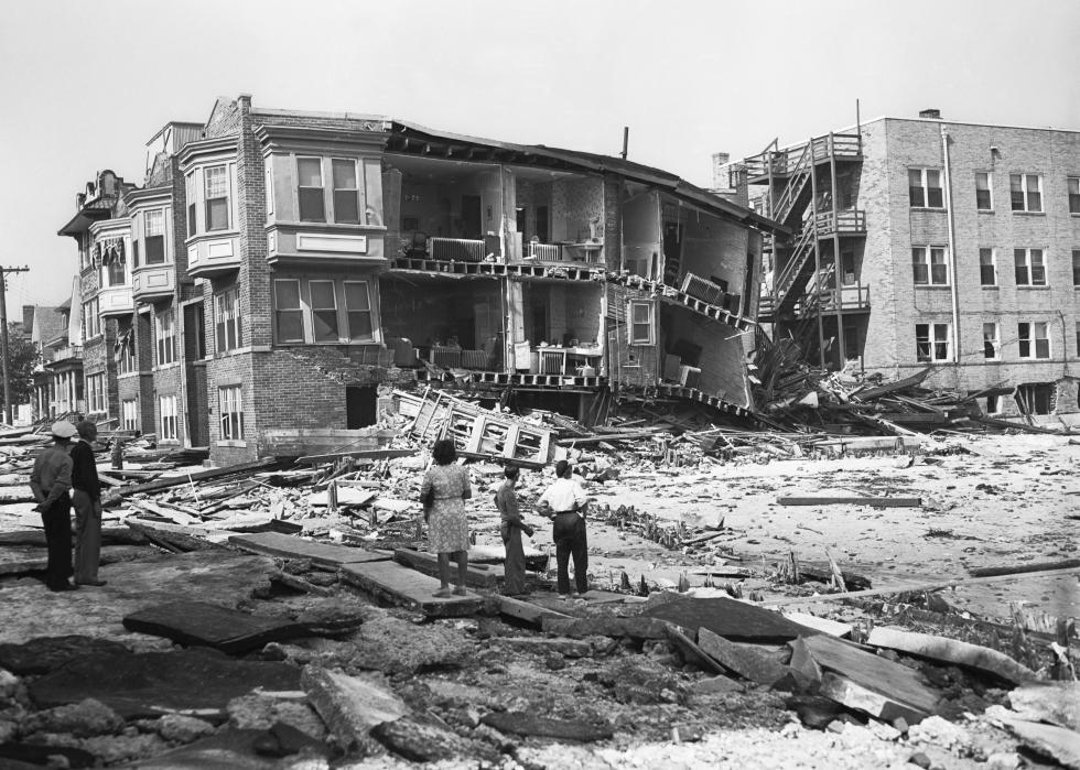 People stand surrounded by wreckage and mostly destroyed buildings.