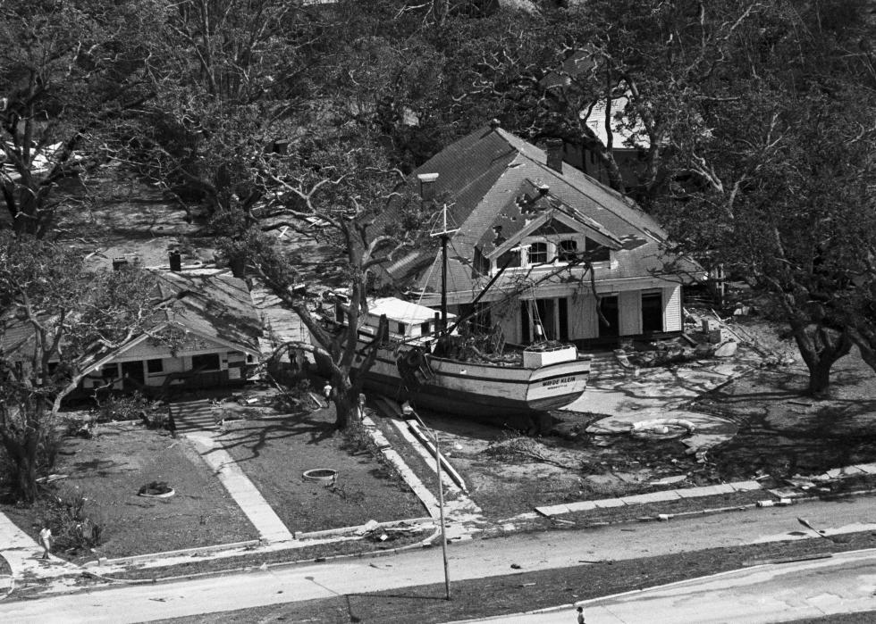 A residential street with two homes destroyed by a storm and surrounded by debris, including a large boat.