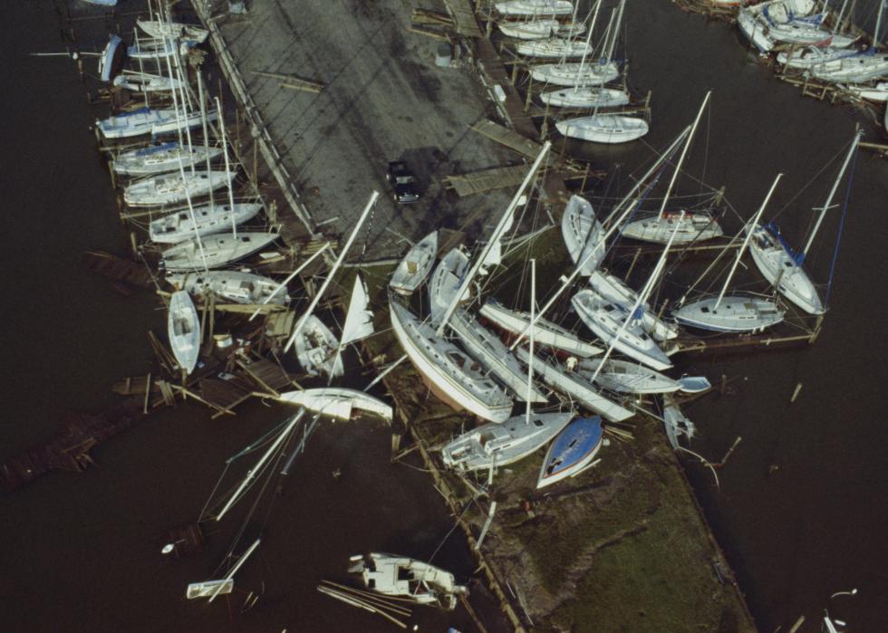 An aerial view of many sailboats docked, with several boats crashed onto the pavement.