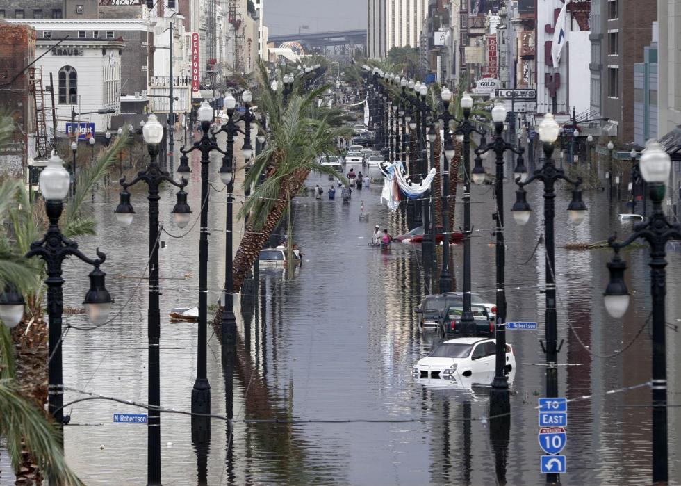 Stalled cars and people standing on an urban street in waist-deep flood water.