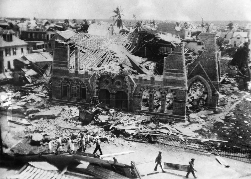 Wreckage surrounding a mostly destroyed building as people walk down the street.