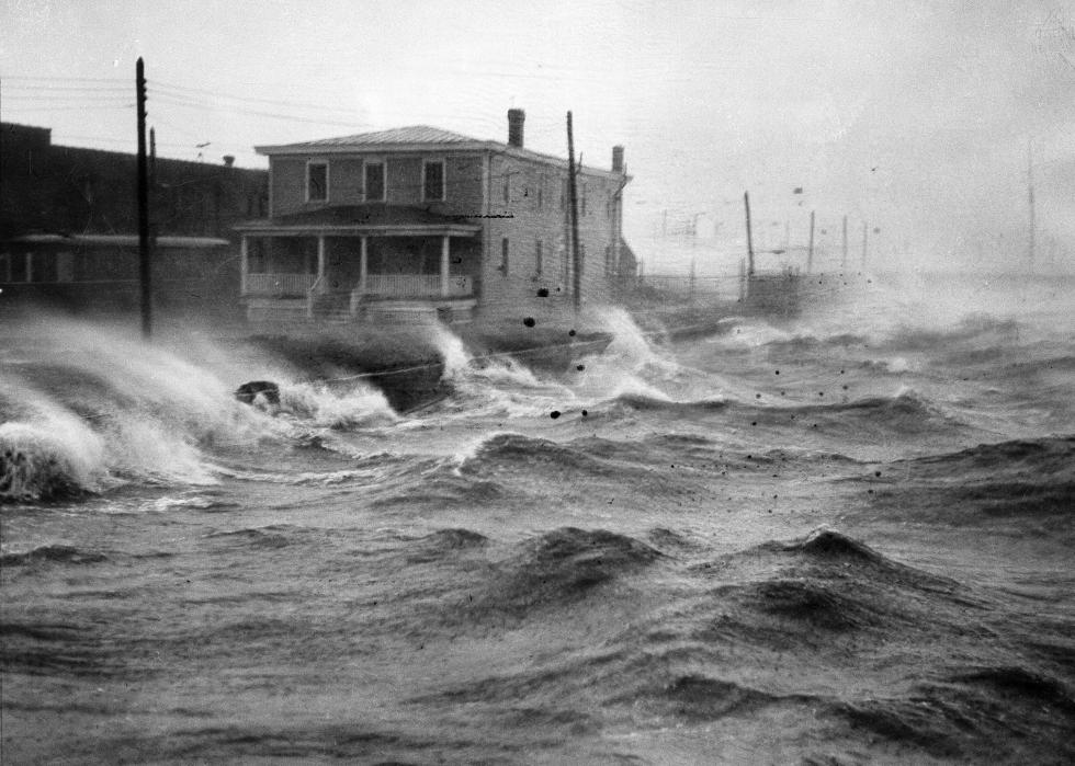 Waves crashing against a street with a house.