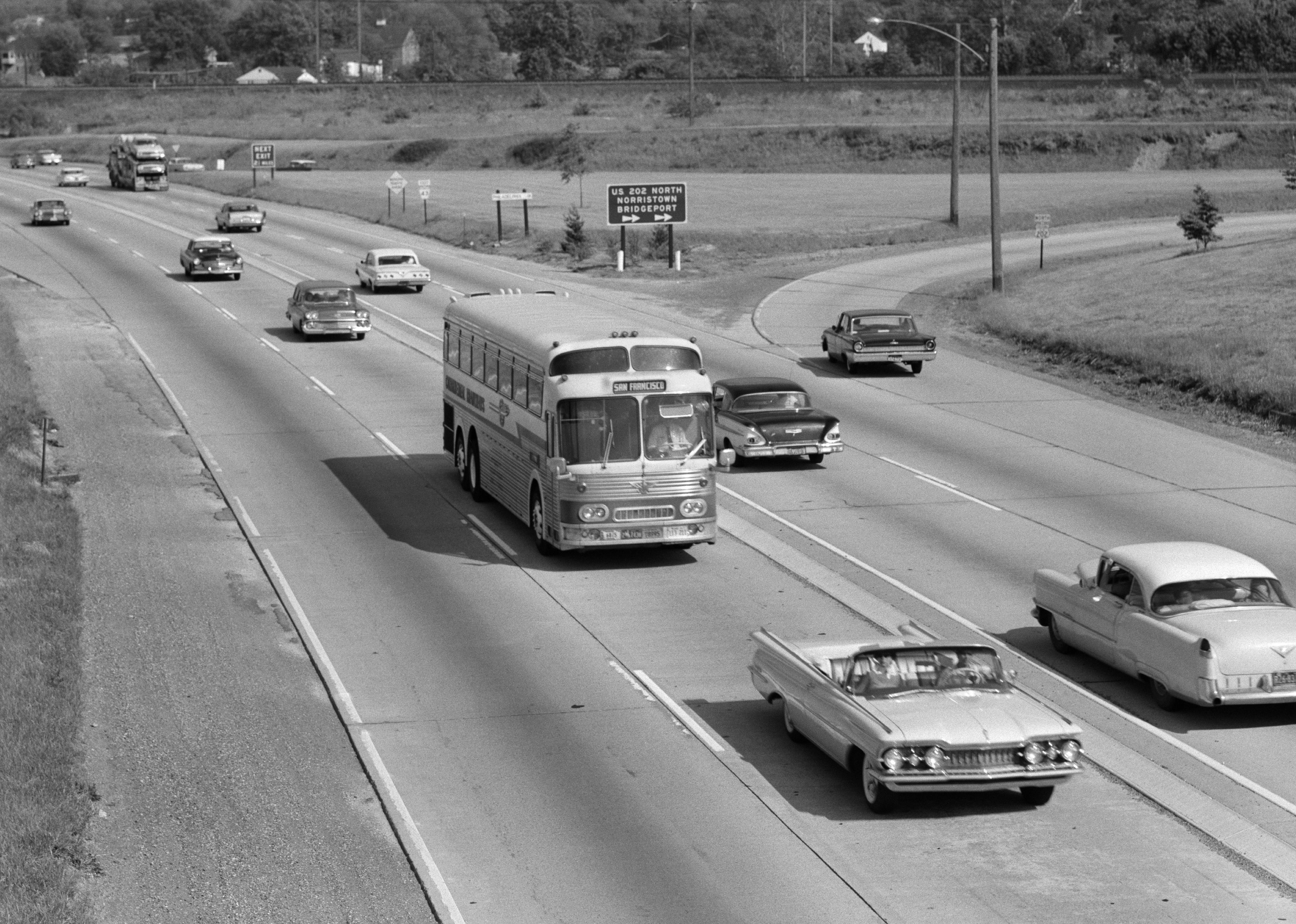 A bus with the words San Francisco on it driving down a busy highway in the 1960s. 