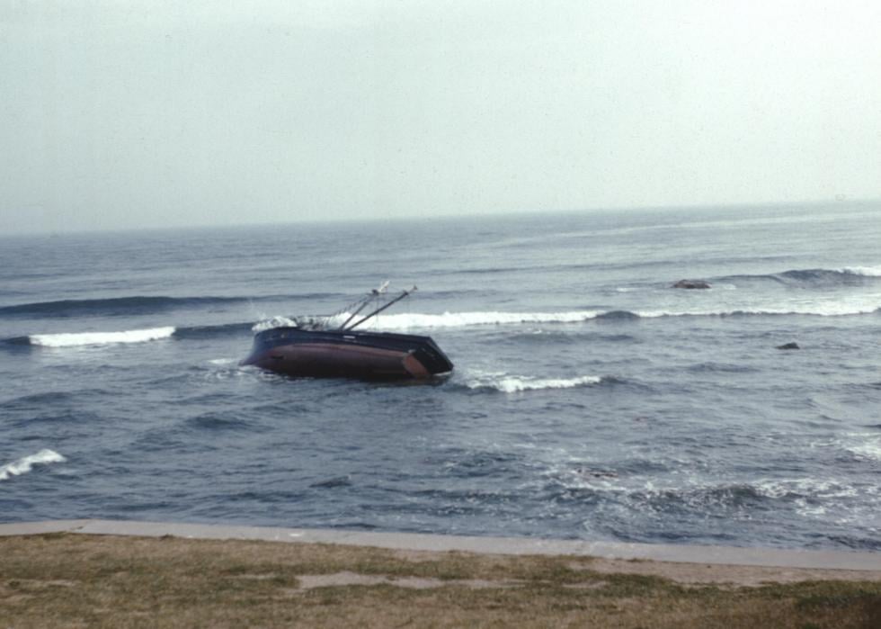 A boat laying on its side in the shallow water near the shoreline. 