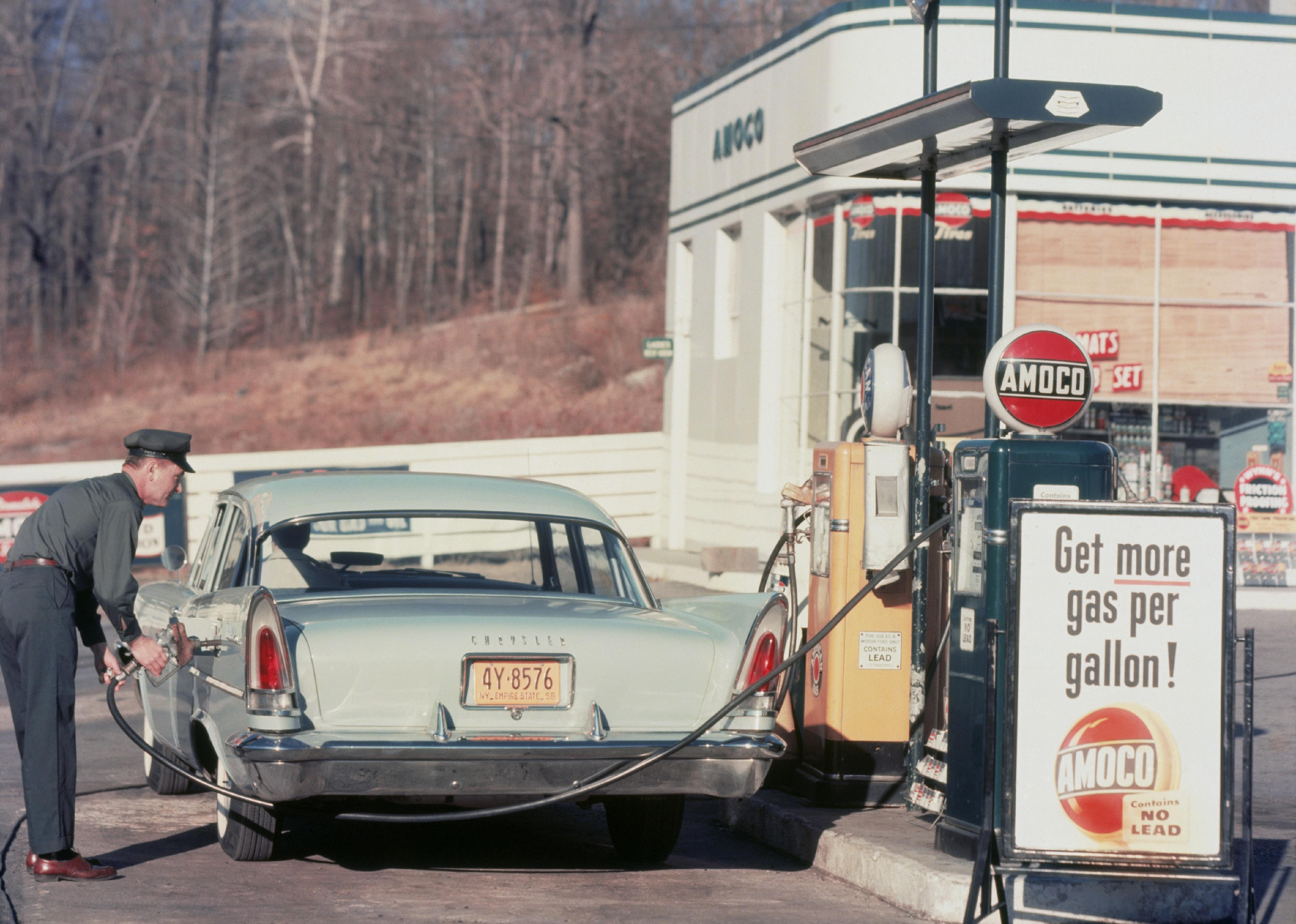 A petrol pump attendant filling up a Chrysler car at an Amoco station, 1958.