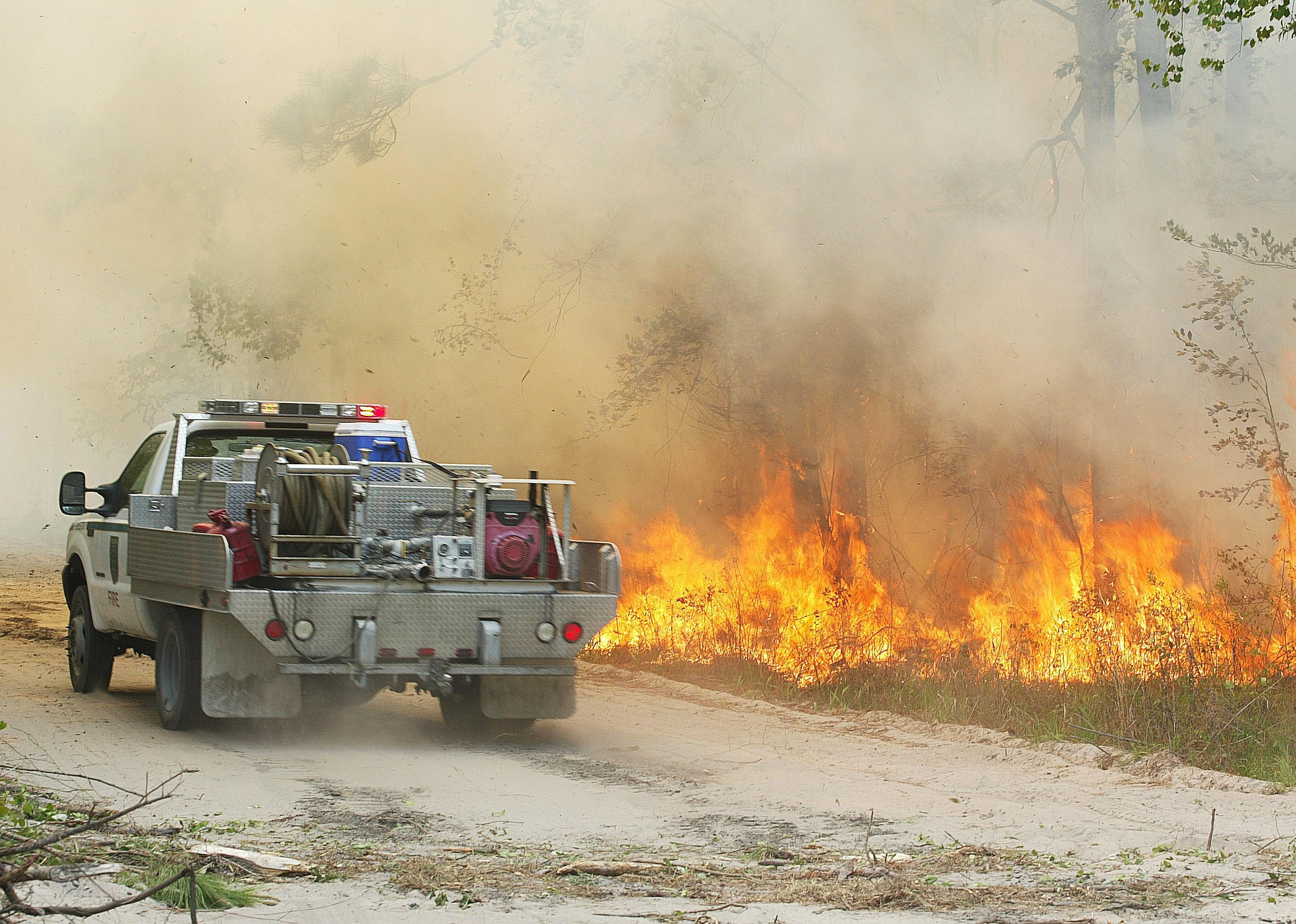 A forest service vehicle drives past a fire burning in a wooded area.