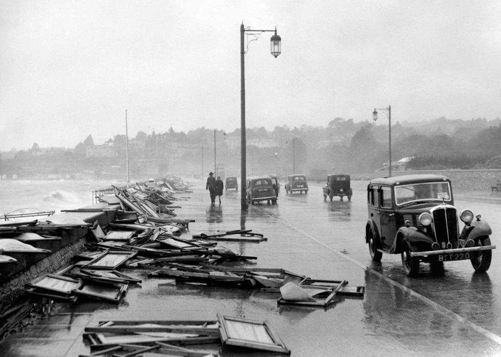 Cars drive down a misty street along a coast with rows of folding street signs blown over.