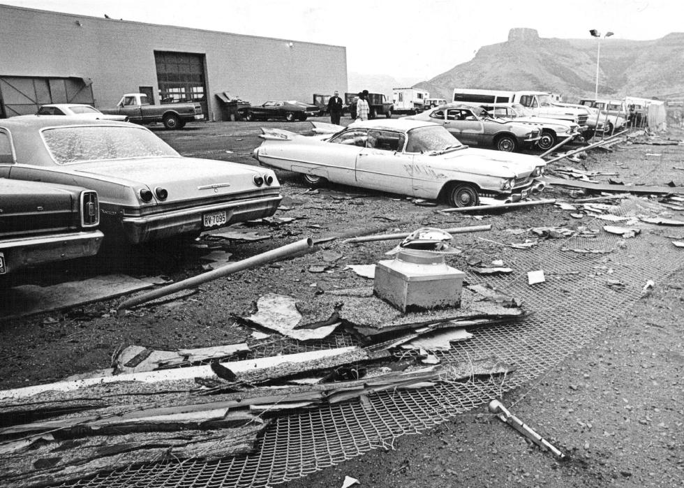 A parking lot with parked cars covered in debris outside a warehouse.