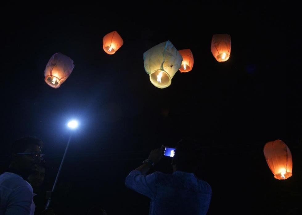 Several lit lanterns float above a couple of people in the dark. 