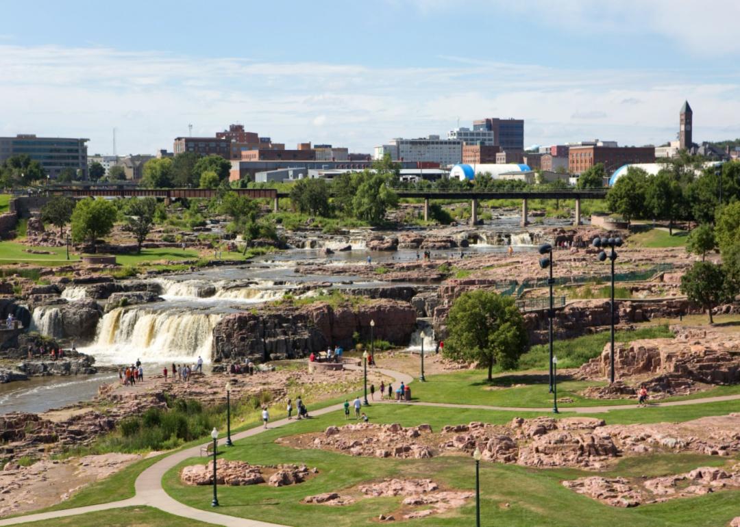 People visiting Falls Park with Sioux Falls skyline in the background.