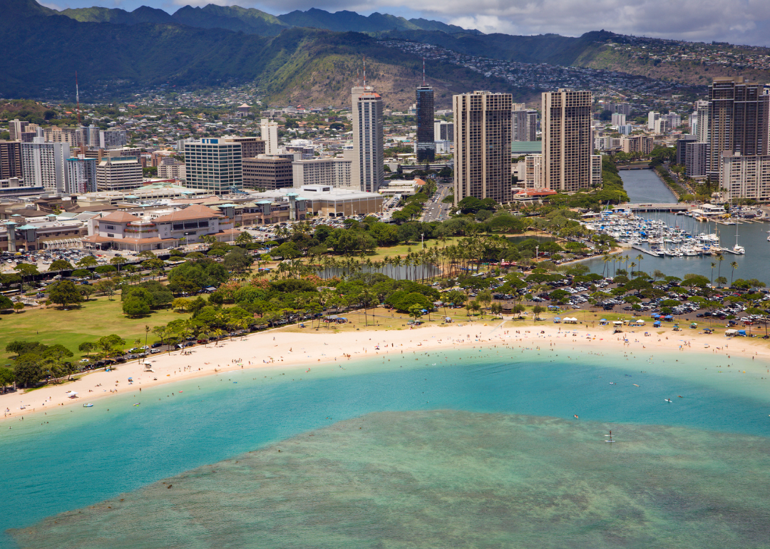An aerial view of downtown Honolulu on the beach with mountains in the background.