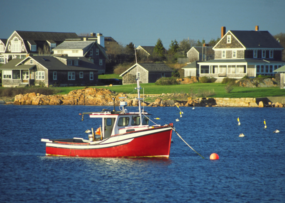 A red fishing boat on the water in front of homes.
